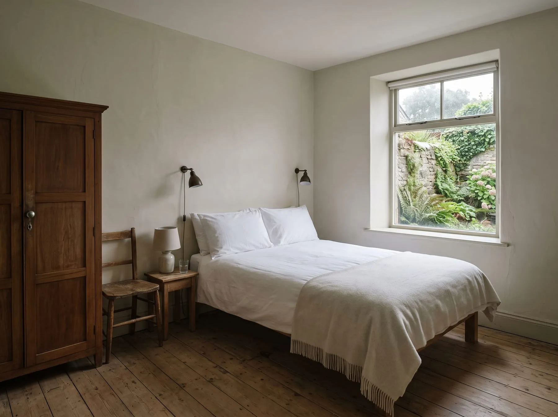 A ground-floor room with a queen bed in white linen, a wooden wardrobe and a window onto the walled garden